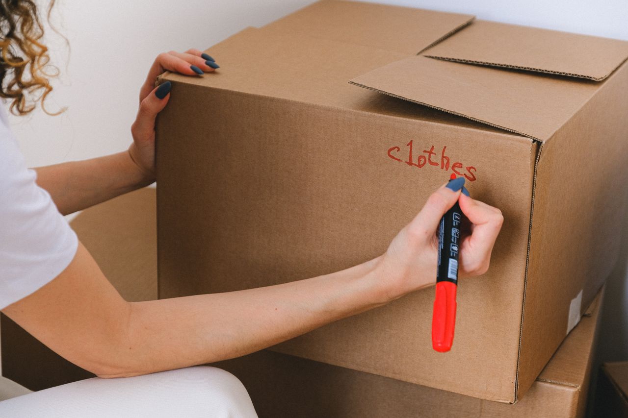 about-us-01 Close-up of a woman labeling a cardboard box with a red marker indoors.
